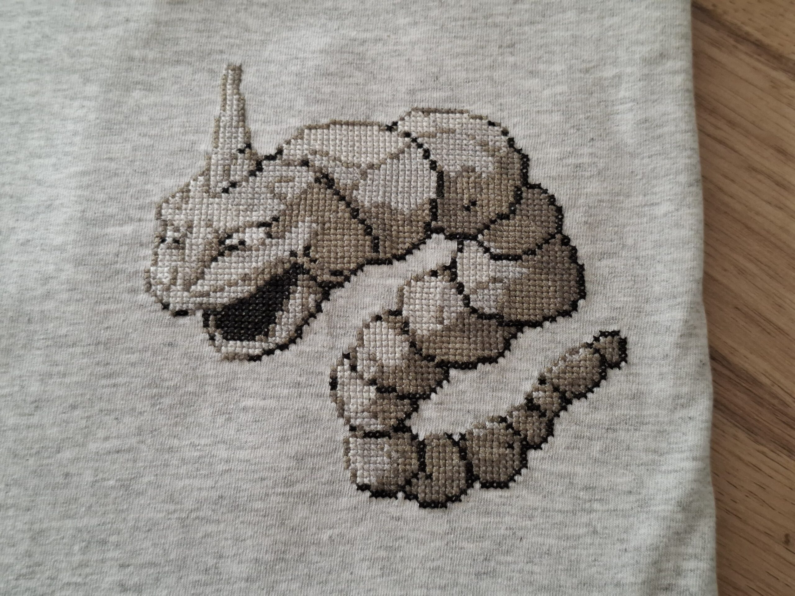 Gros plan sur la broderie. T-shirt onix plié, posé sur une table en bois.